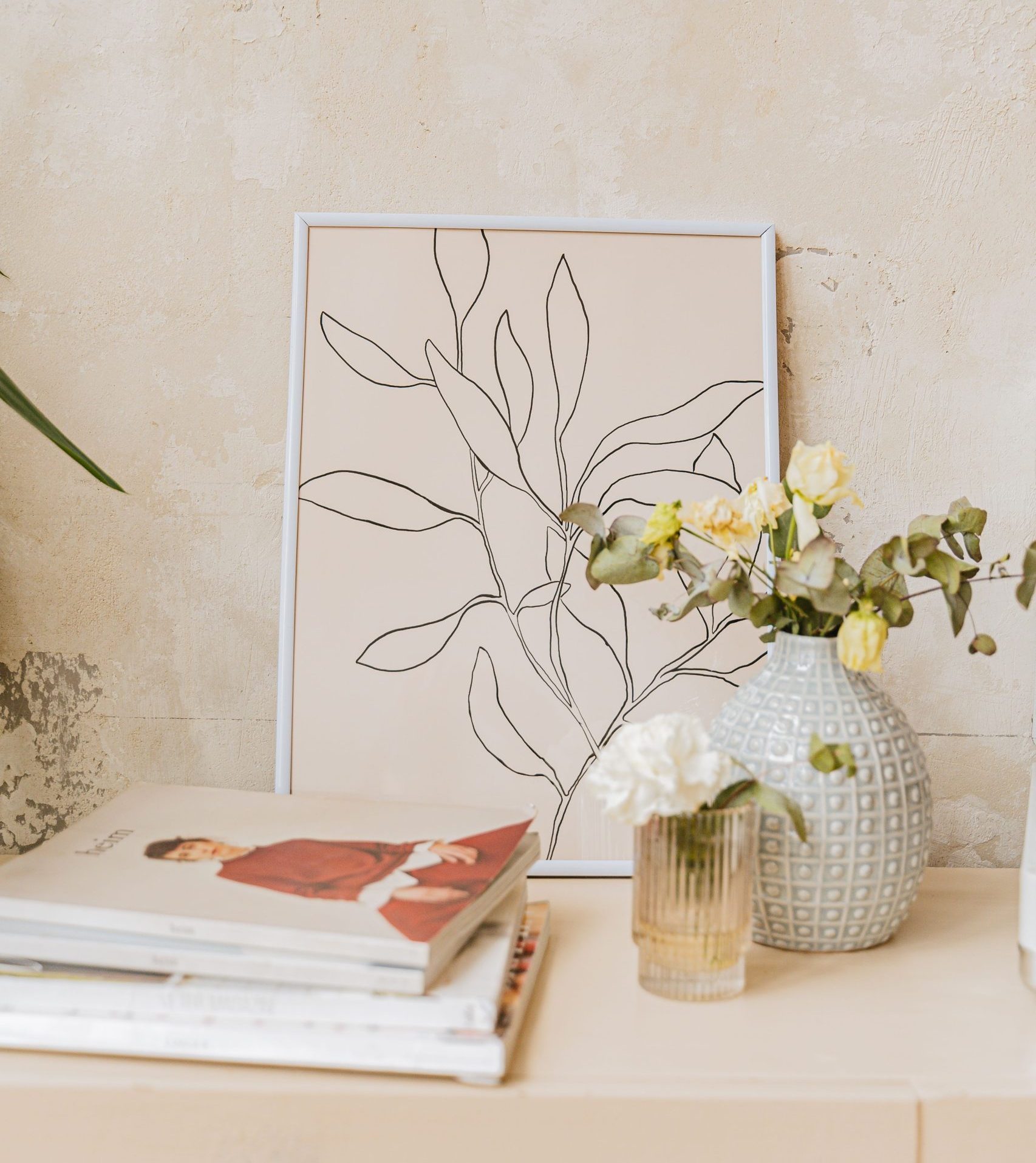 A minimalist interior featuring art and a floral vase on a table.